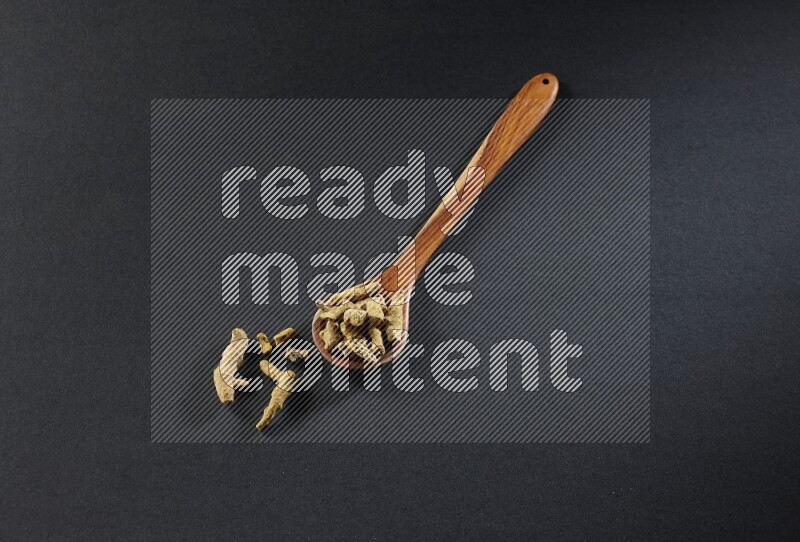 A wooden ladle full of dried turmeric fingers on black flooring