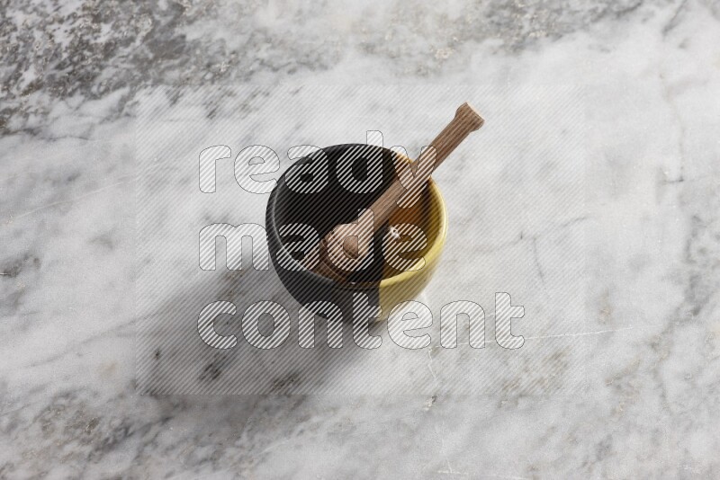 Multicolored pottery bowl with wooden honey dipper in it on grey marble background