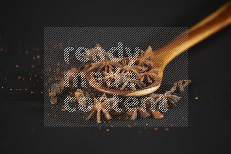 Star Anise in a wooden spoon ladle with more anise on black flooring