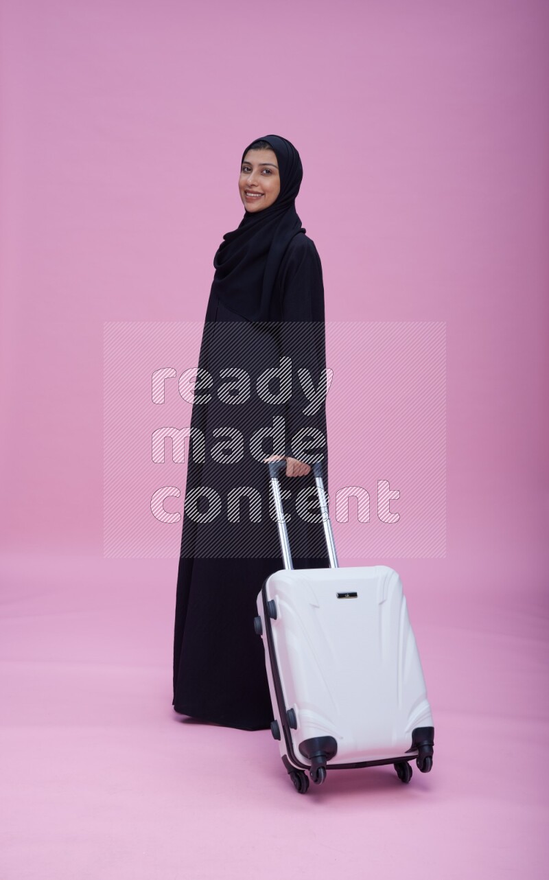 Saudi woman wearing Abaya standing holding bag on pink background