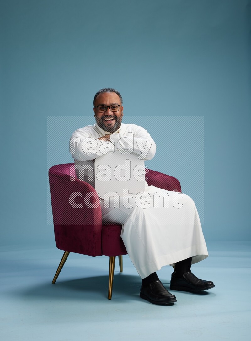 Saudi Man without shimag sitting on chair holding social media sign on blue background