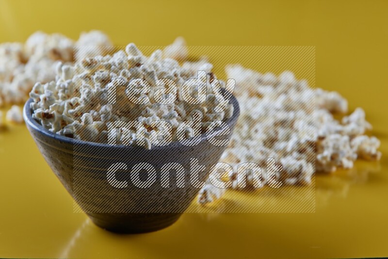 A multicolored pottery bowl full of popcorn with popcorn beside it on a yellow background in different angles