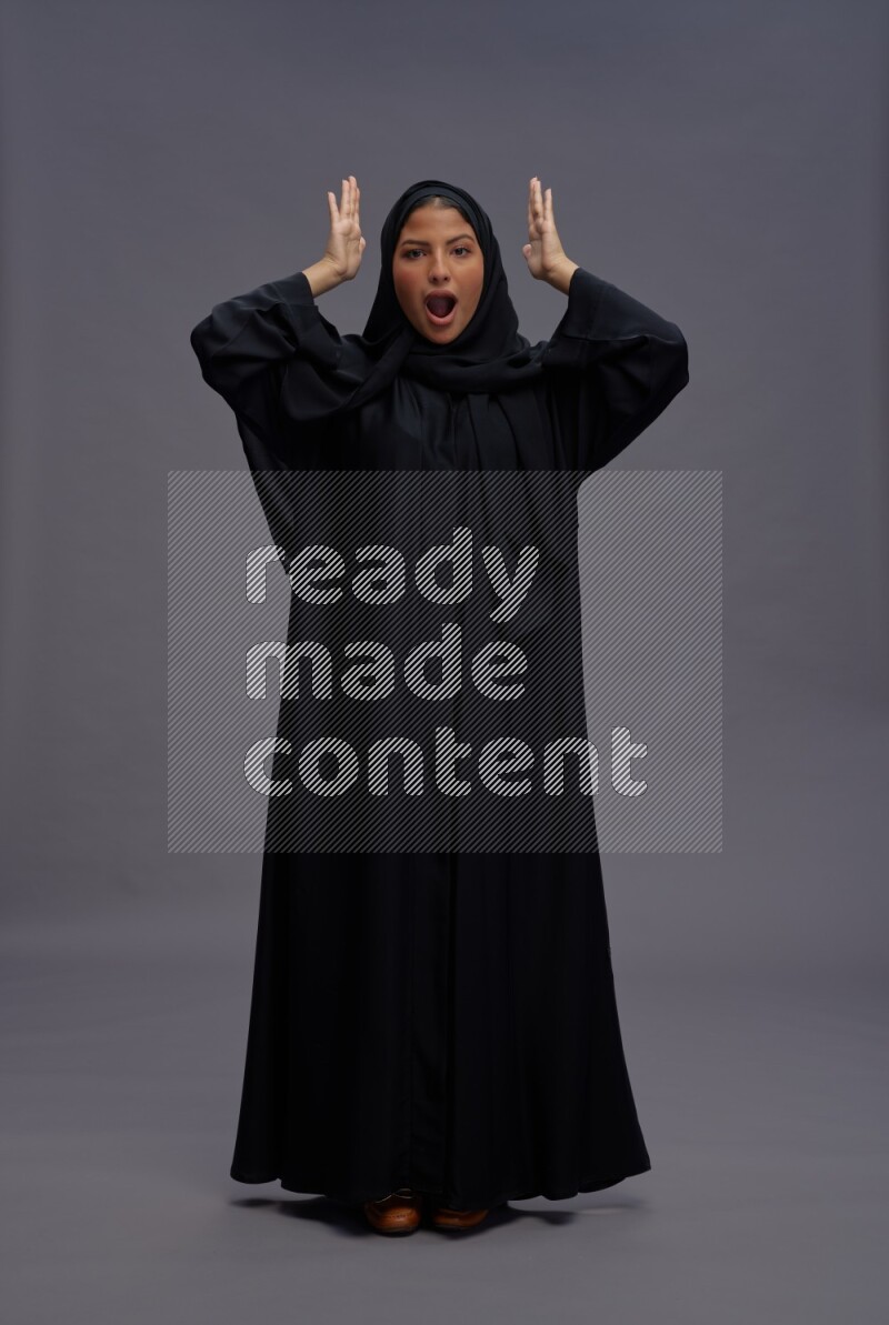 Saudi woman wearing Abaya standing hands behind head on gray background