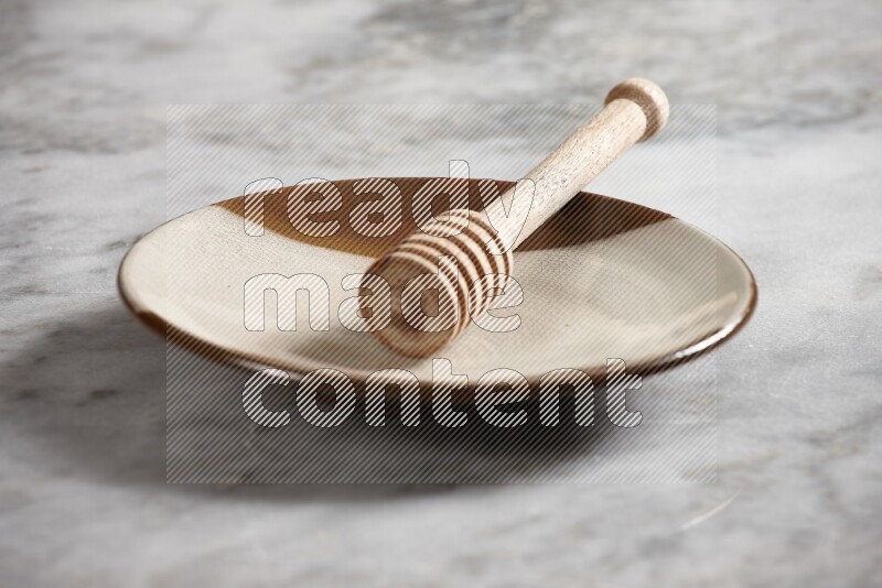 Multicolored pottery plate with wooden honey dipper in it on grey marble background