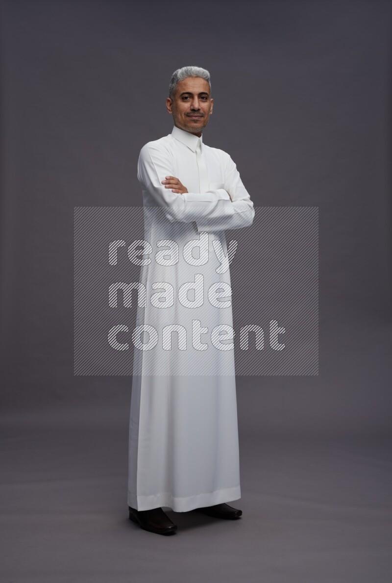 Saudi man wearing thob standing with crossed arms on gray background