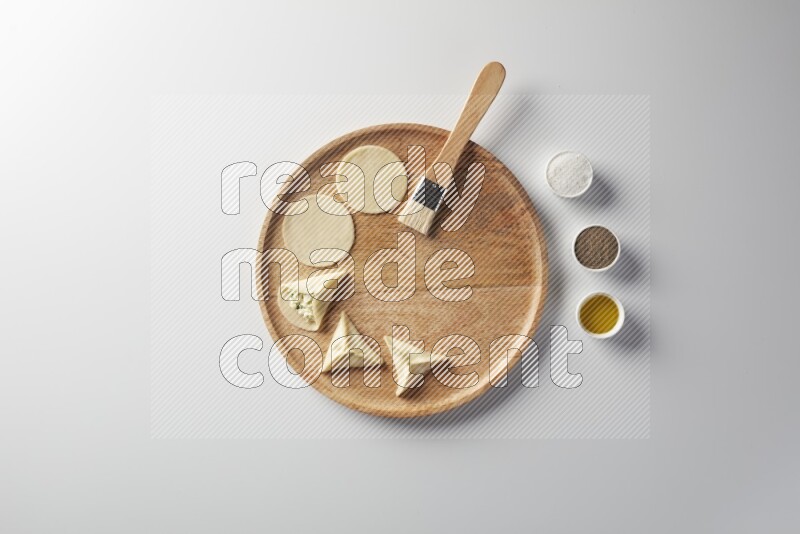two closed sambosas and one open sambosa filled with cheese while salt, black pepper and oil with oil brush aside in a wooden dish on a white background