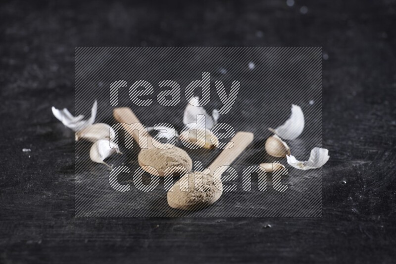 ملعقتان خشبيتان مملوءتان بمسحوق الثوم، محاطتان بفصوص الثوم المقشرة وقشرتها على خلفية سوداء