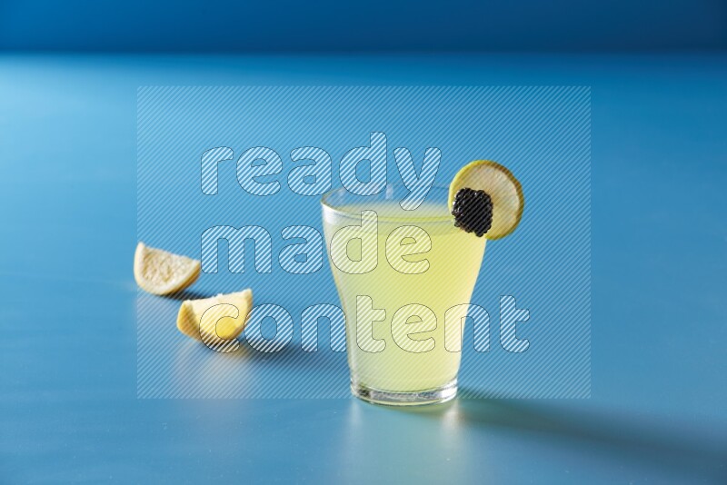 glass of lemon juice with lemon slice and berry on blue background