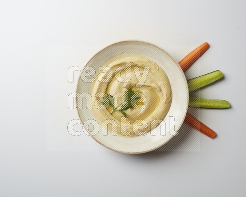 Hummus in a pottry plate garnished with parsley on a white back ground