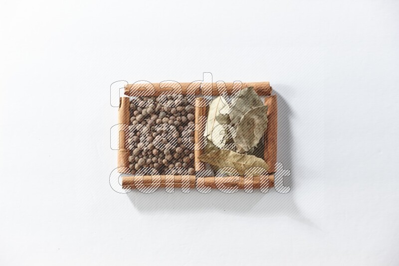 مربعان من أعواد القرفة ممتلئان ببهار الفلفل الحلو وأوراق الغار علي خلفية بيضاء
