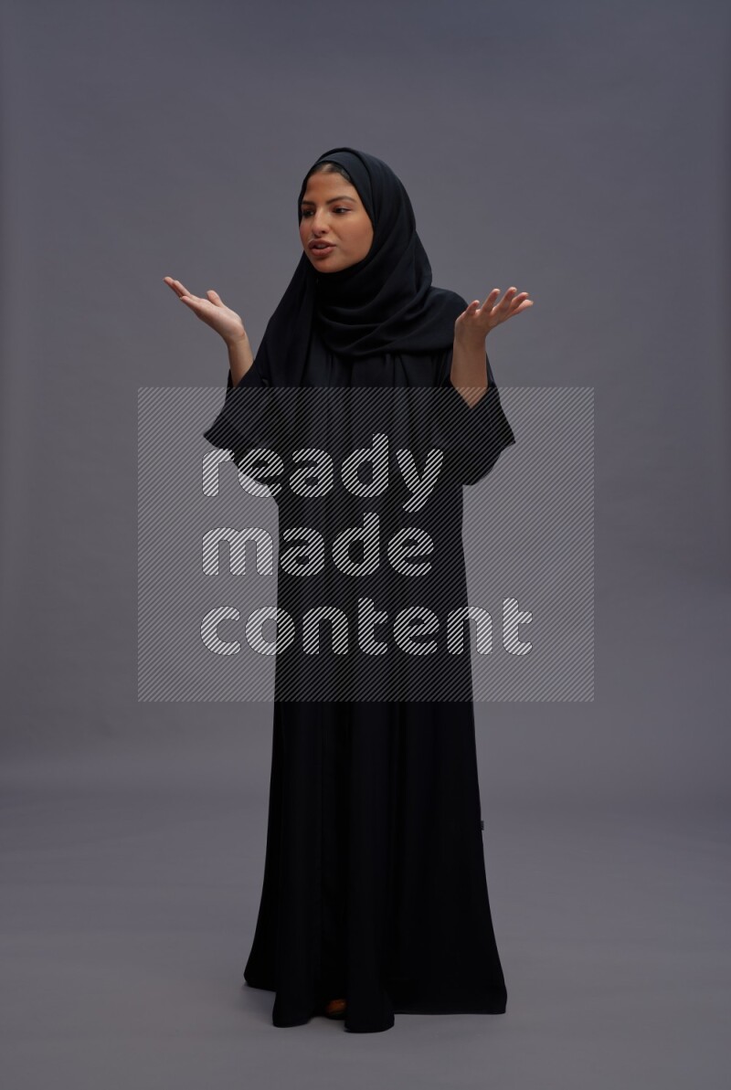 Saudi woman wearing Abaya standing interacting with the camera on gray background