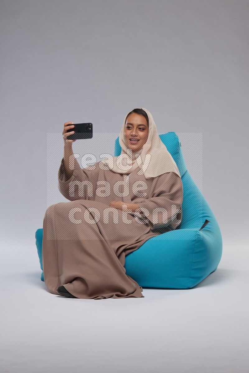 A Saudi woman sitting on a blue beanbag and taking selfie
