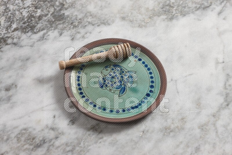 Decorative pottery plate with wooden honey dipper in it on grey marble background