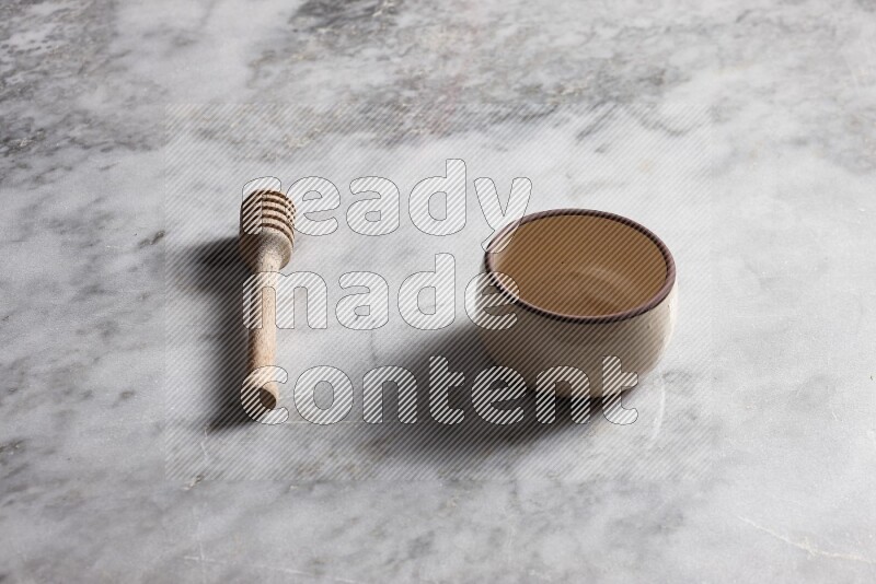 Beige pottery bowl with wooden honey dipper on the side on grey marble background