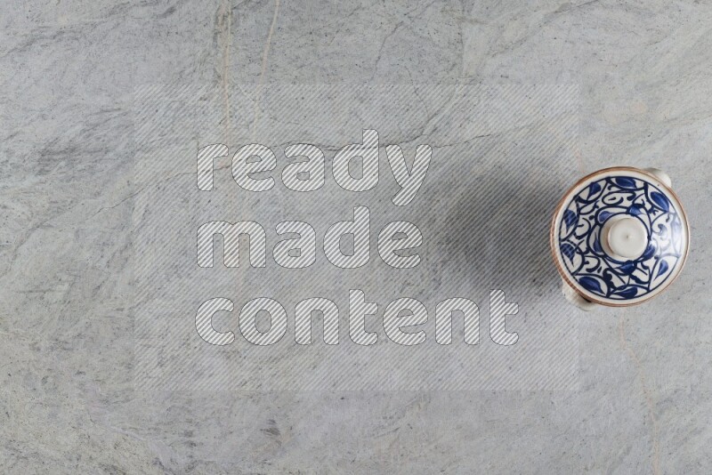 A multicolored pottery pot with its lid on grey marble background