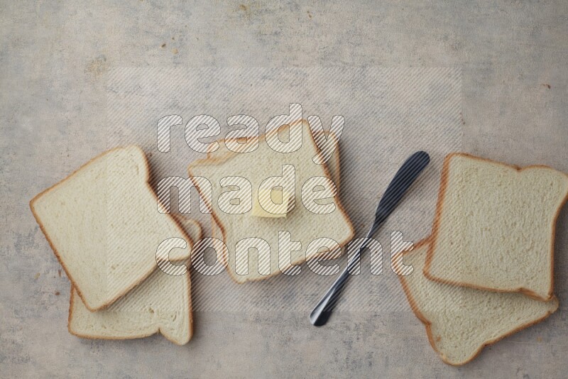 White toast slices with a butter cube and a spreading knife on a light blue textured background