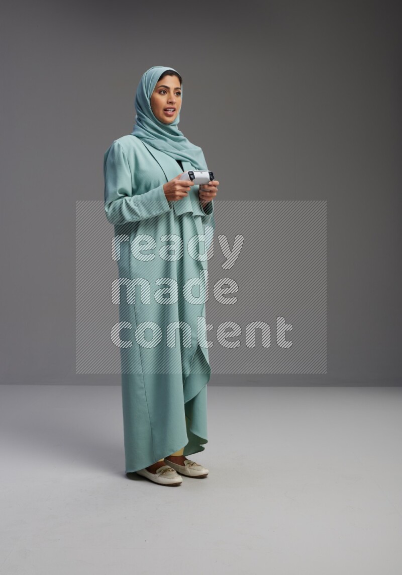 Saudi Woman wearing Abaya standing Playing Games on Gray background