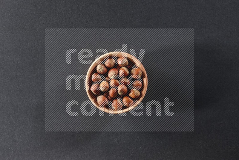 A wooden bowl full of hazelnuts on a black background in different angles