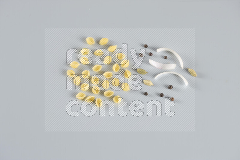 Raw pasta with different ingredients such as cherry tomatoes, garlic, onions, red chilis, black pepper, white pepper, bay laurel leaves, rosemary, cardamom and mushrooms on light blue background