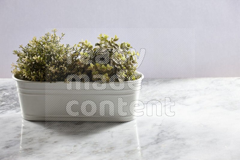 Multiple green artificial plants in white pot on grey marble background