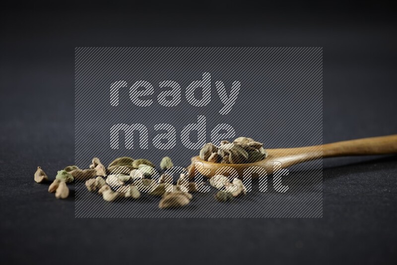 A wooden spoon full of cardamom on black flooring