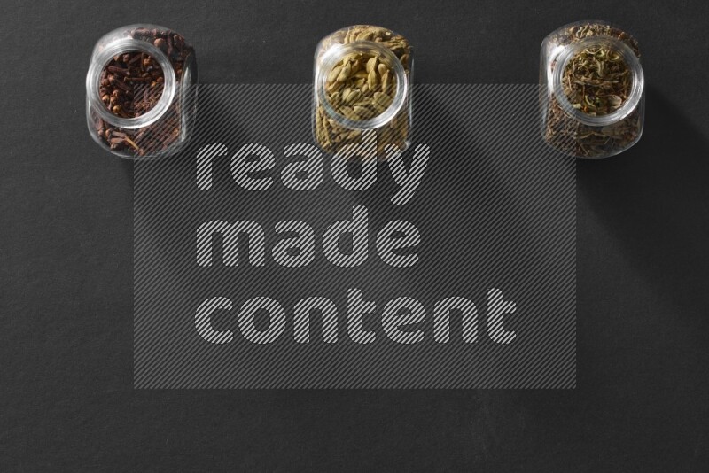 قرنفل وحبوب الهيل و ريحان مجفف في أوعية زجاجية علي خلفية سوداء