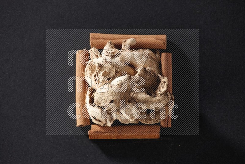 A single square of cinnamon sticks full of dried ginger on black flooring