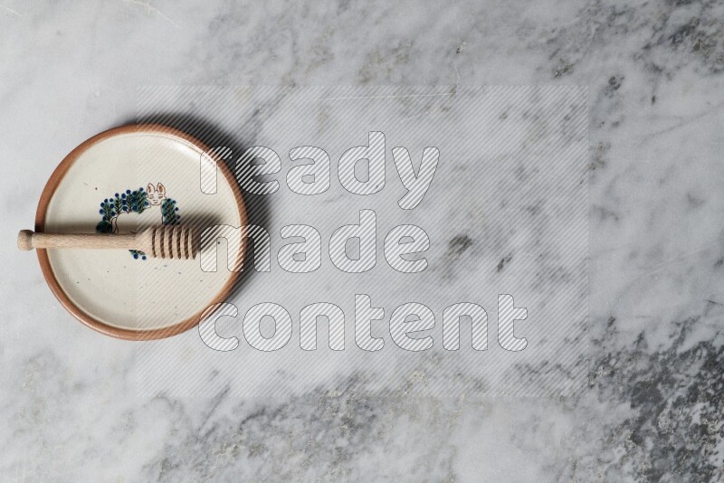 Decorative pottery plate with wooden honey dipper in it on grey marble background