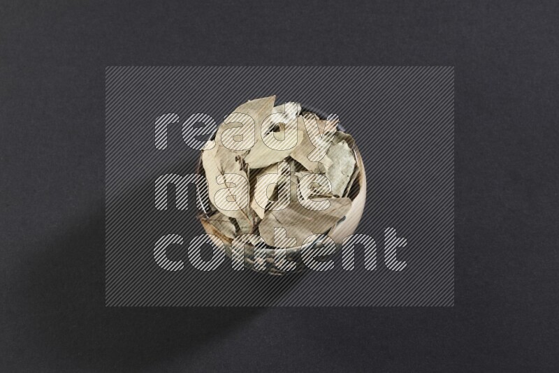 A multicolored pottery bowl full of dried bay leaves on black flooring