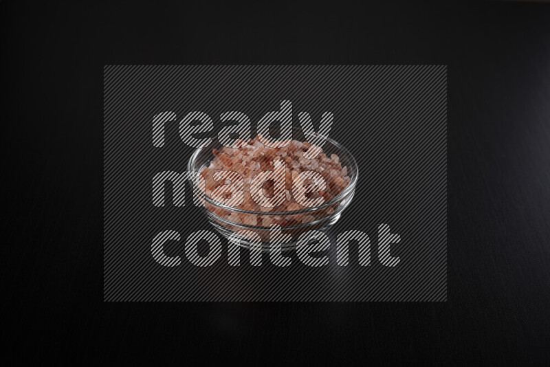 A glass bowl full of coarse himalayan salt crystals on black background
