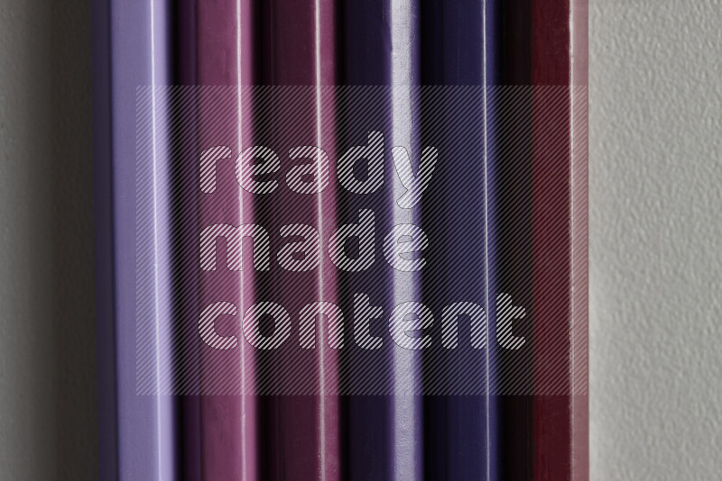 A collection of colored pencils arranged showcasing a gradient of purple hues on grey background