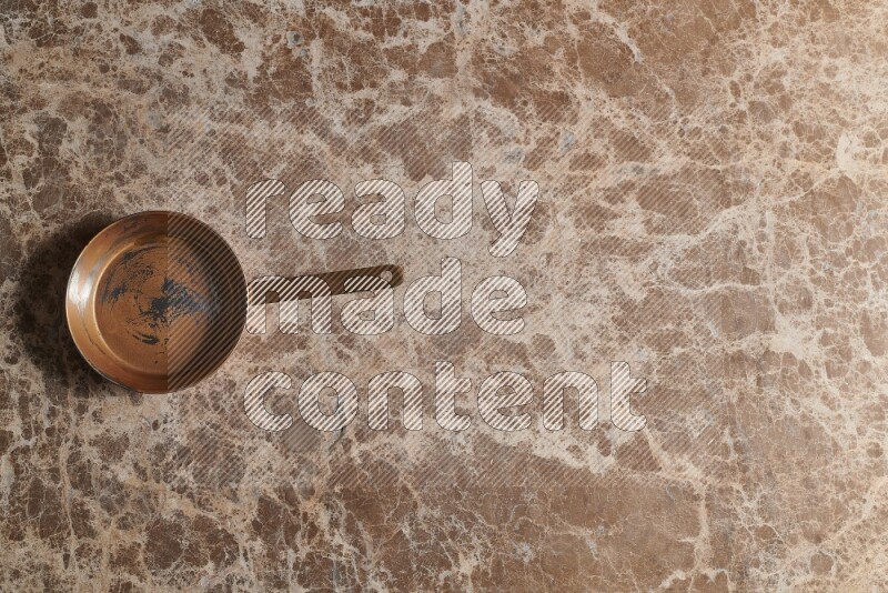 A small copper pan on beige marble background