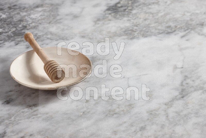 طبق فخاري بيج مع ملعقة عسل خشبية بداخله على خلفية من الرخام الرمادي