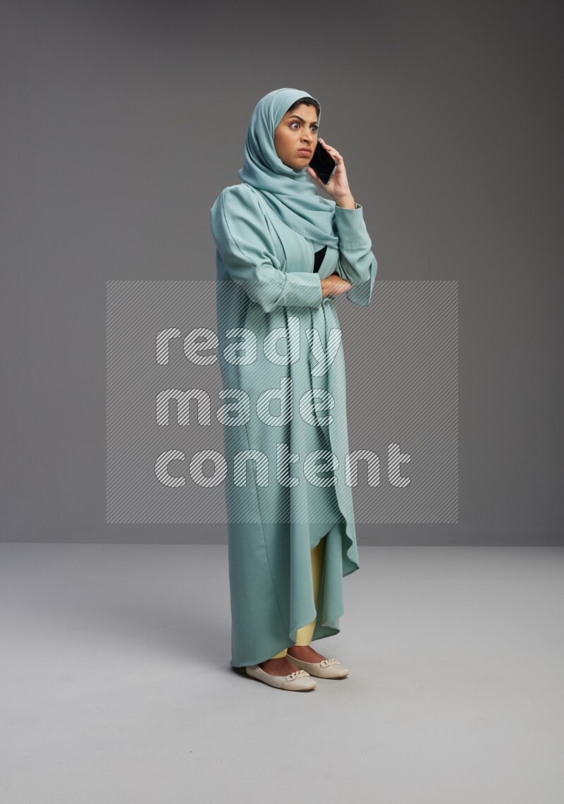Saudi Woman wearing Abaya standing talking on phone on Gray background