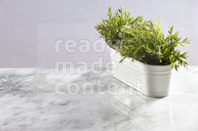 Multiple green artificial plants in white pot on grey marble background