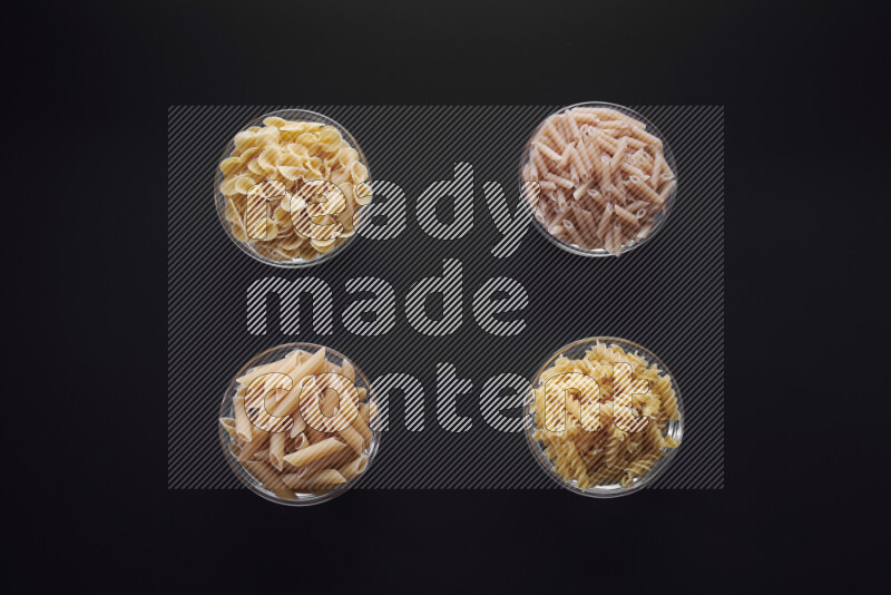 Different pasta types in glass bowls on black background