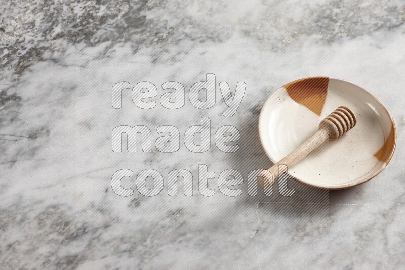 Multicolored pottery plate with wooden honey dipper in it on grey marble background