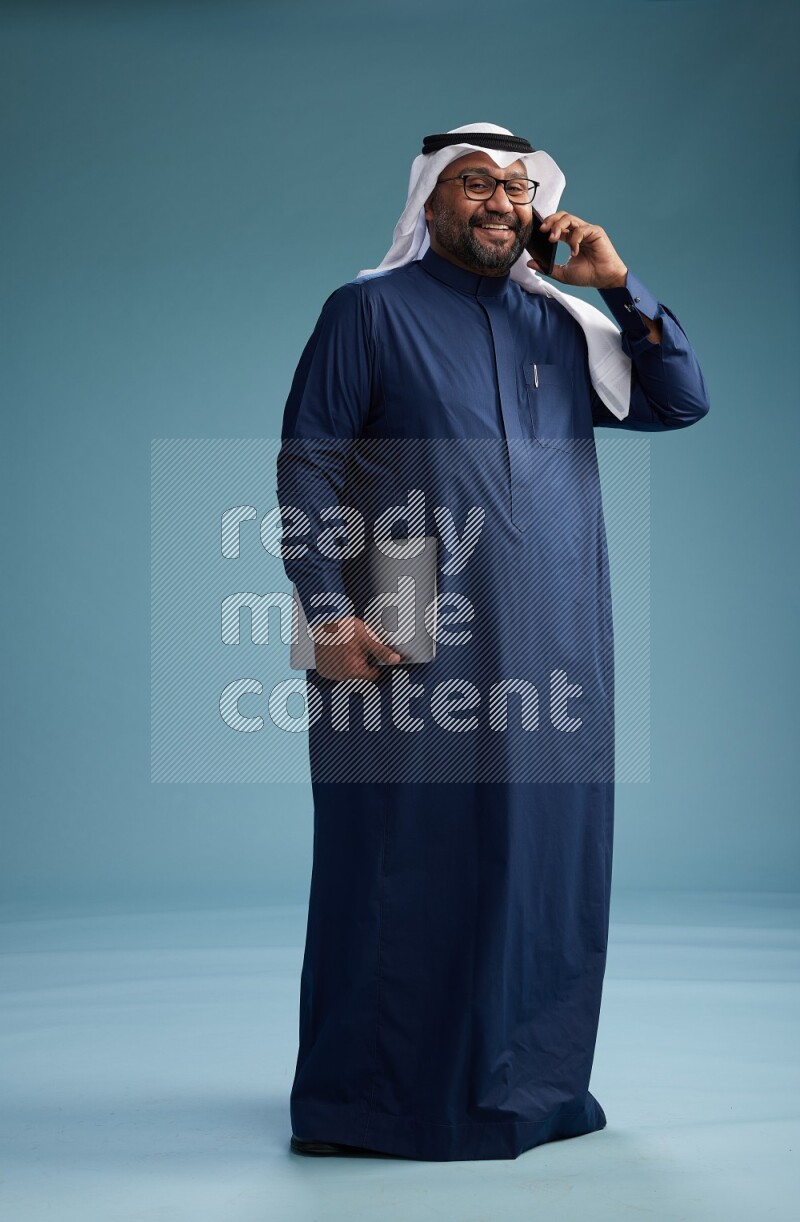 Saudi Man with shimag Standing talking on phone on blue background