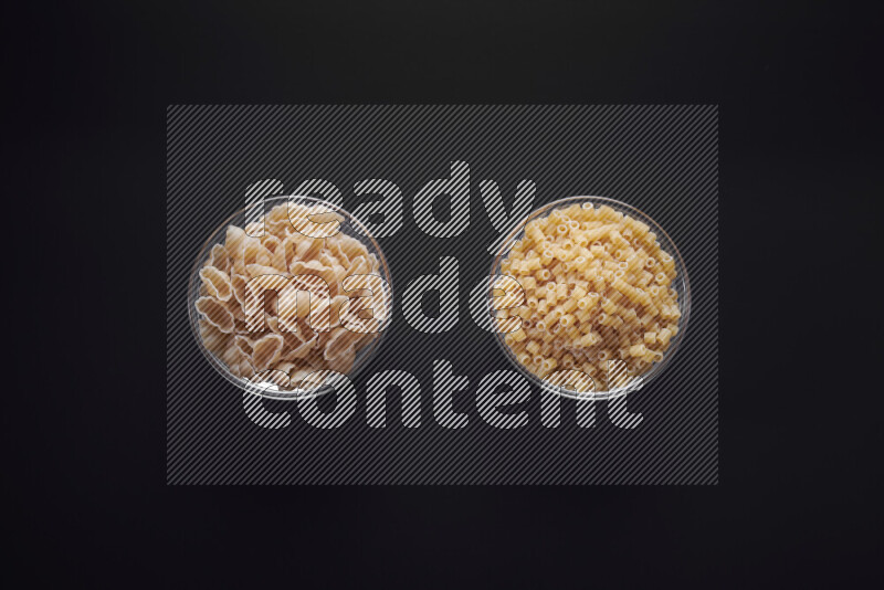 Different pasta types in glass bowls on black background