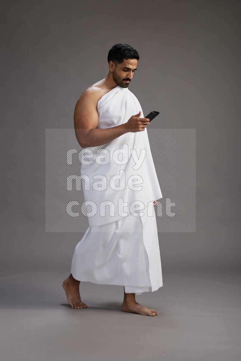 A man wearing Ehram Standing texting on phone on gray background