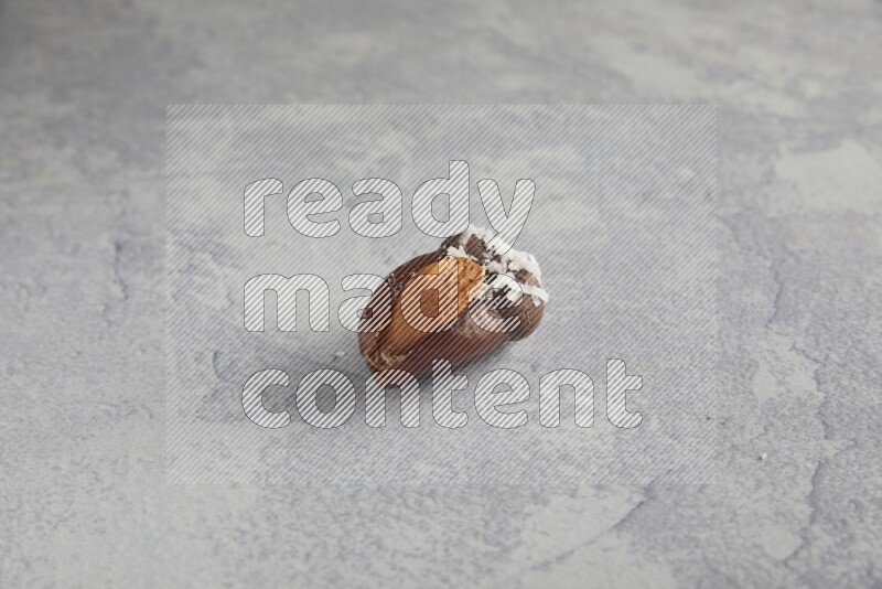 Almond stuffed date covered with dark chocolate and coconut on a light grey background