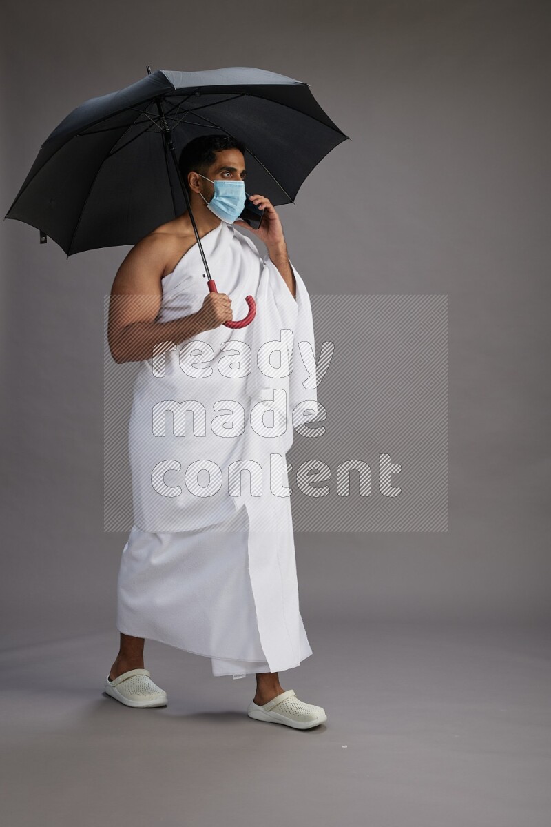 A man wearing Ehram and mask Standing holding umbrella on gray background on gray background