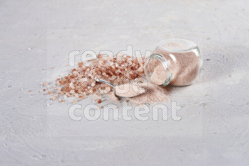 A glass jar full of fine himalayan salt with some himalayan crystals beside it on a white background