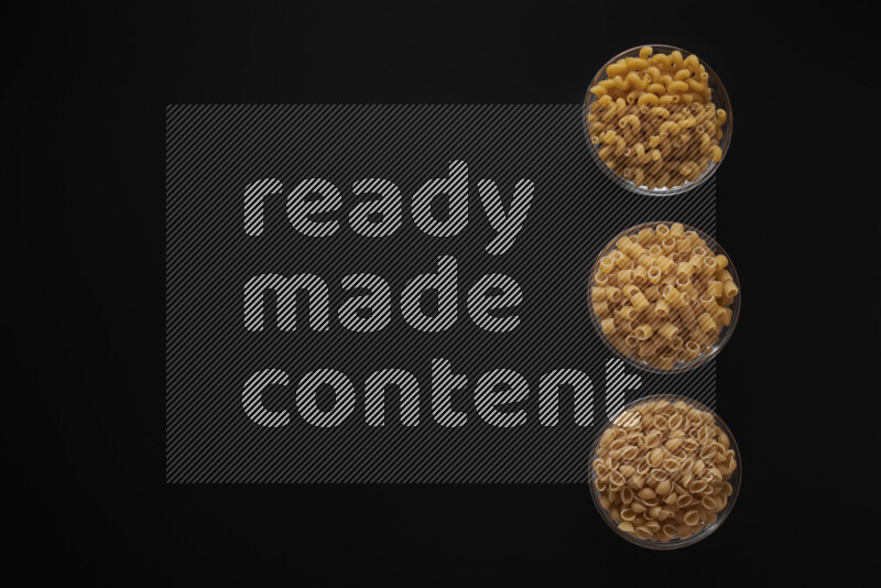 Different pasta types in 3 glass bowls on black background