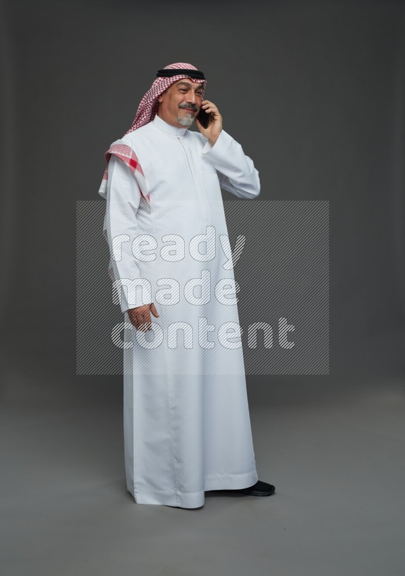 Saudi man with shomag Standing talking on phone on gray background