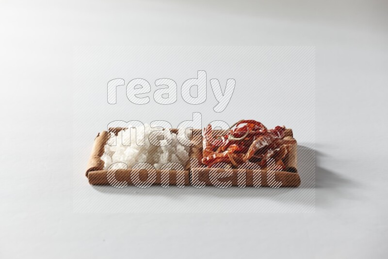 2 squares of cinnamon sticks full of dried red chilis and white salt on white flooring