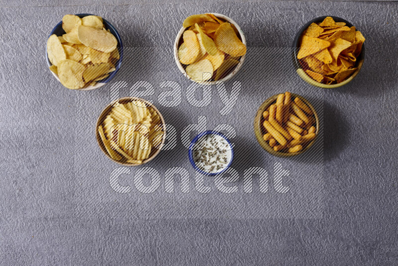Assorted snacks in pottery bowls on grey background