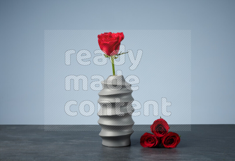 An arrangement of vivid red roses in a grey spiral vase on black marble background
