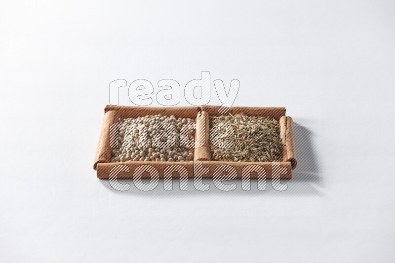 مربعان من أعواد القرفة ممتلئان بحبوب الفلفل الأبيض وحبوب الكمون علي خلفية بيضاء