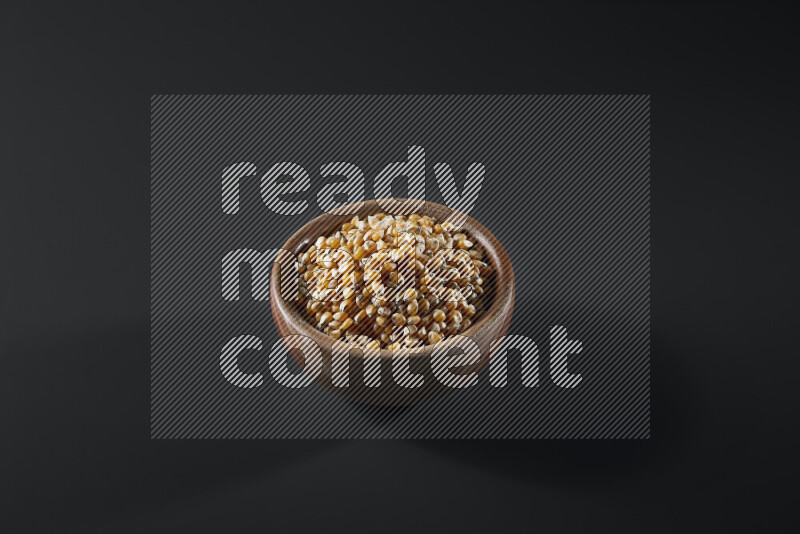 Dry corn kernels in a wooden bowl on grey background